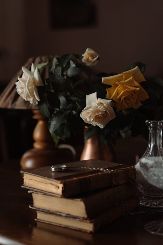 Vase of white and yellow roses next to stack of antique books